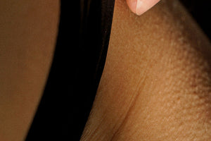 Close-up of a person's hip and upper thigh area wearing sheer black fishnet stockings, with fingers lifting the fabric to show the texture and transparency.