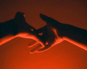 Silhouetted human hands reaching toward each other against a glowing red-orange gradient background.